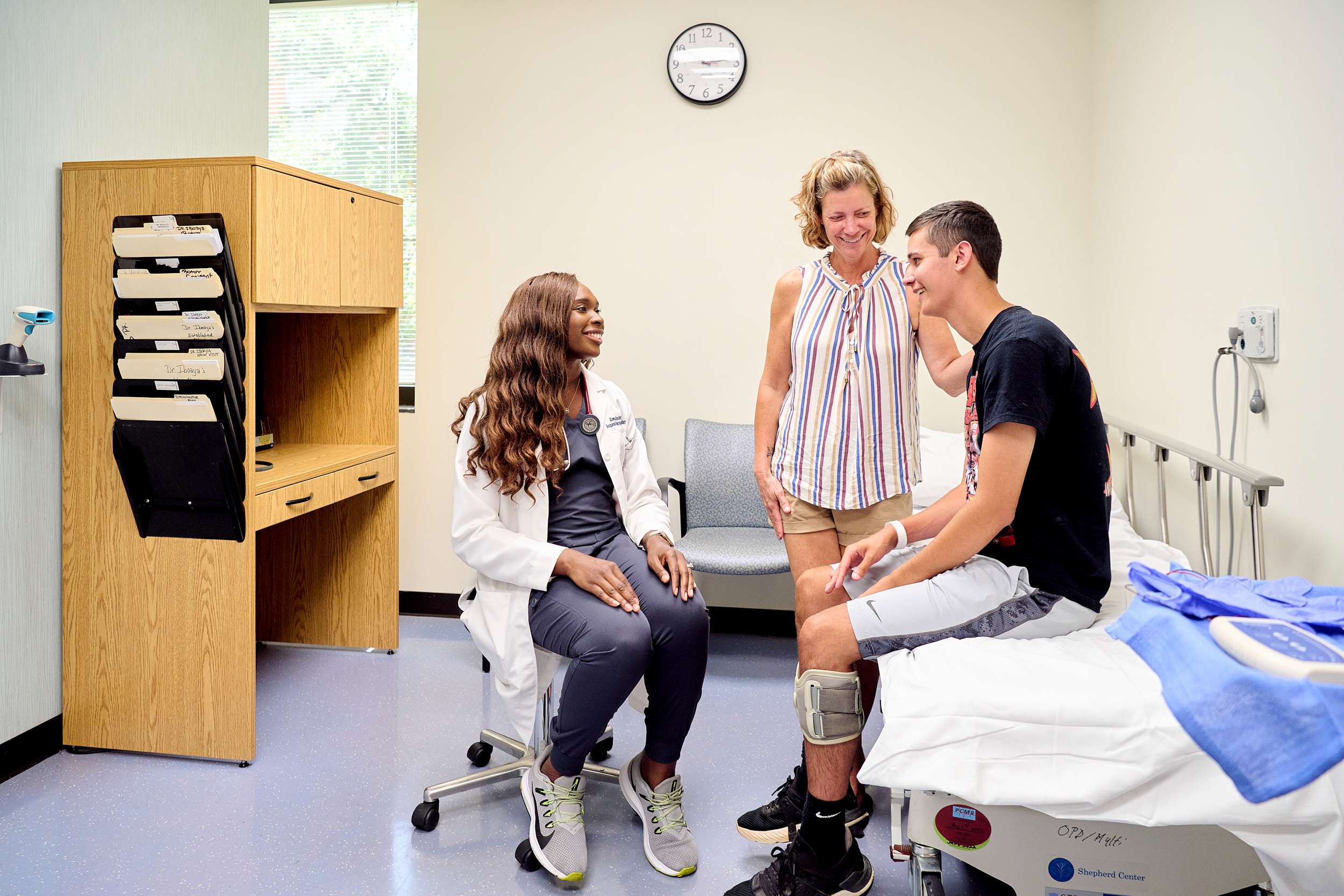 Male patient alongside his mother meets with physician for continued outpatient medical management and rehabilitative care following the completion of an inpatient rehabilitation program for a brain injury.